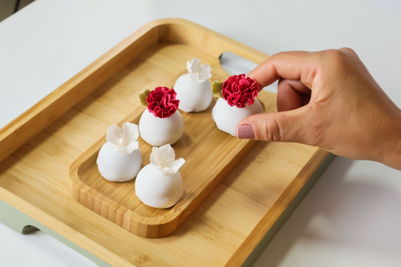 Mão arrumando doces finos com flores de açúcar em uma tábua