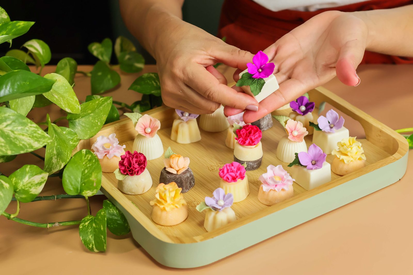 Mão colocando doce fino com flor de açúcar em bandeja com folhas