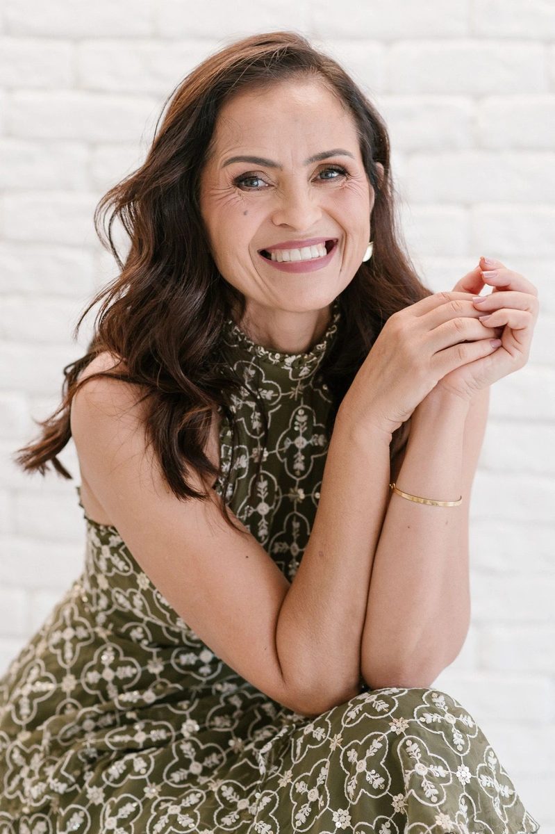Prof Gi Carvalho sorrindo, sentada, de vestido verde