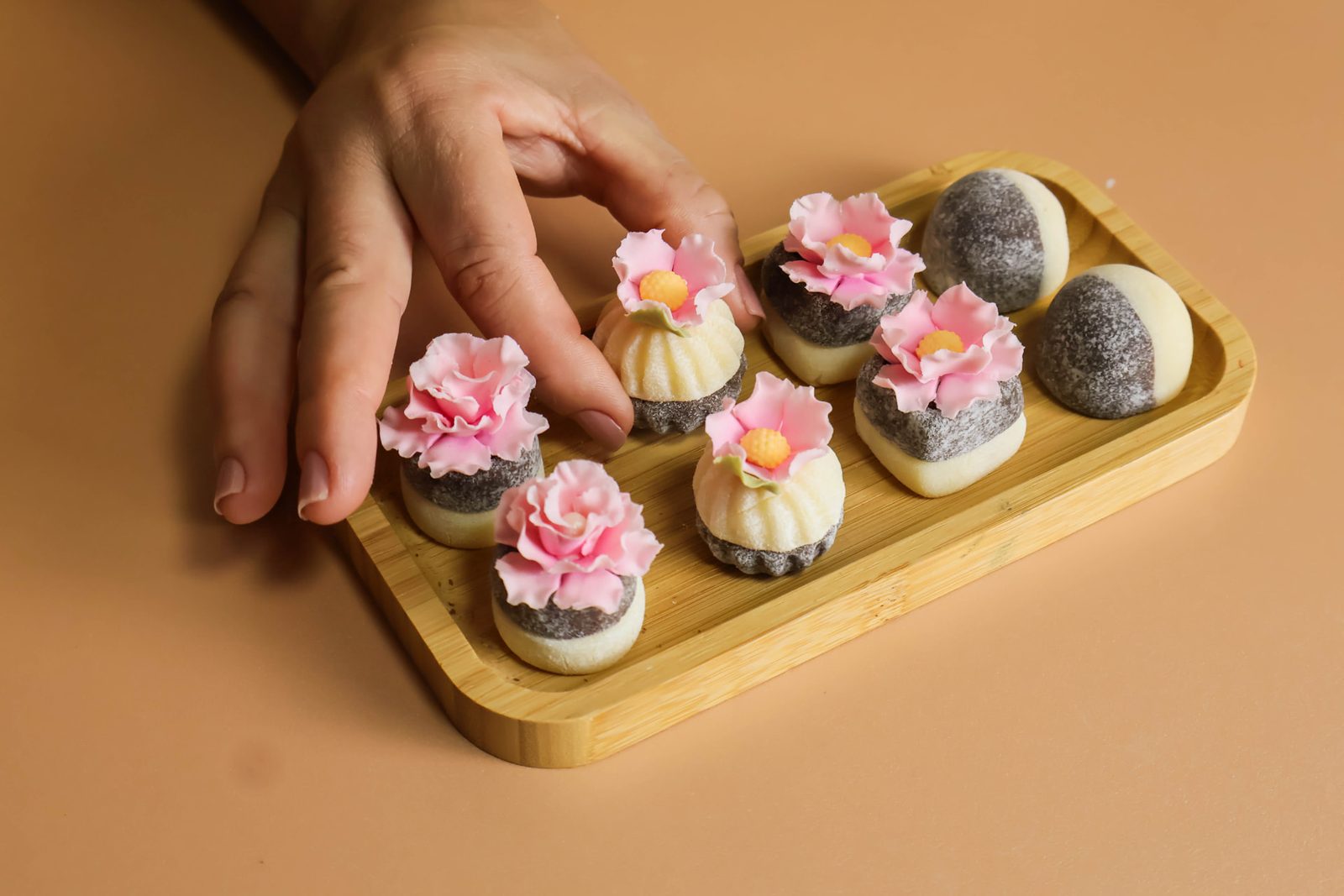 Mão tocando doces finos rosa e brancos com flor de açúcar no centro