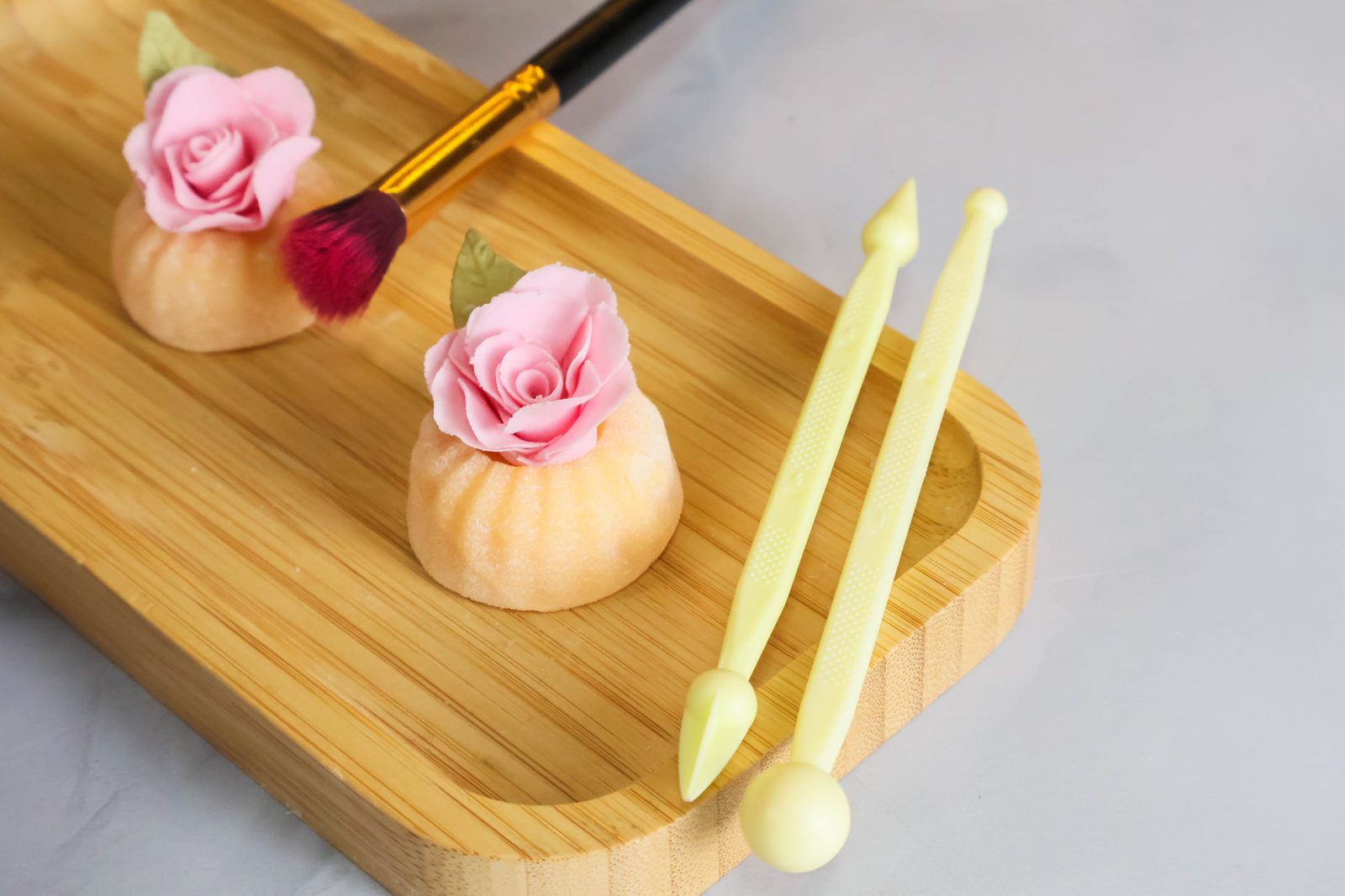 Doces com rosas de açúcar rosa sobre tábua de bambu com pincel e ferramentas
